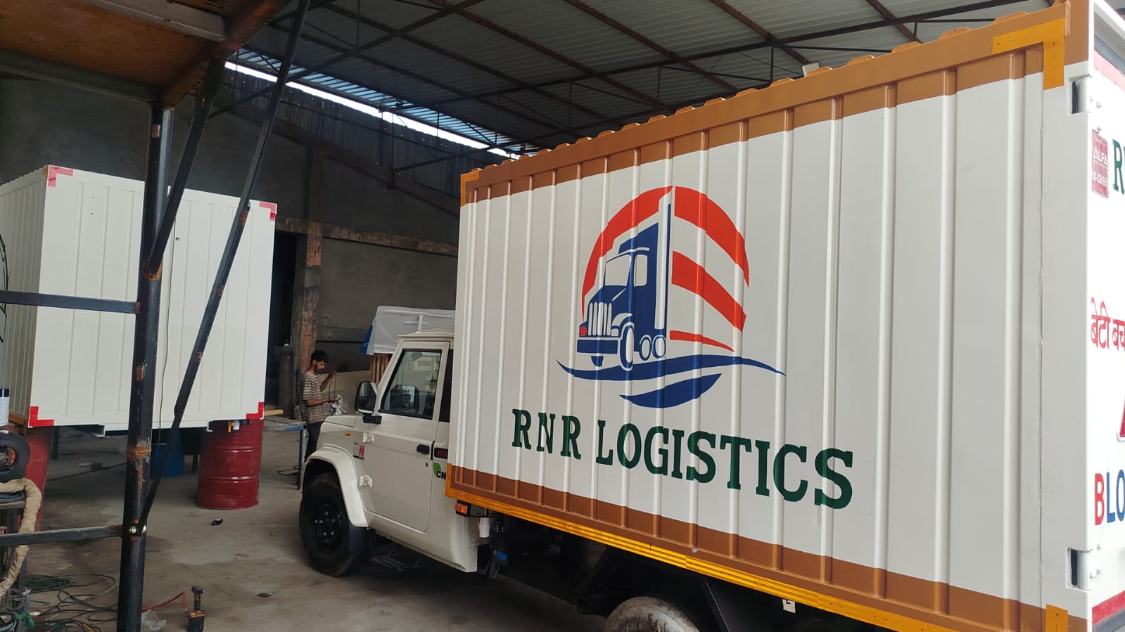 An RNR Logistics branded white and ochre cargo truck photographed inside a workshop.